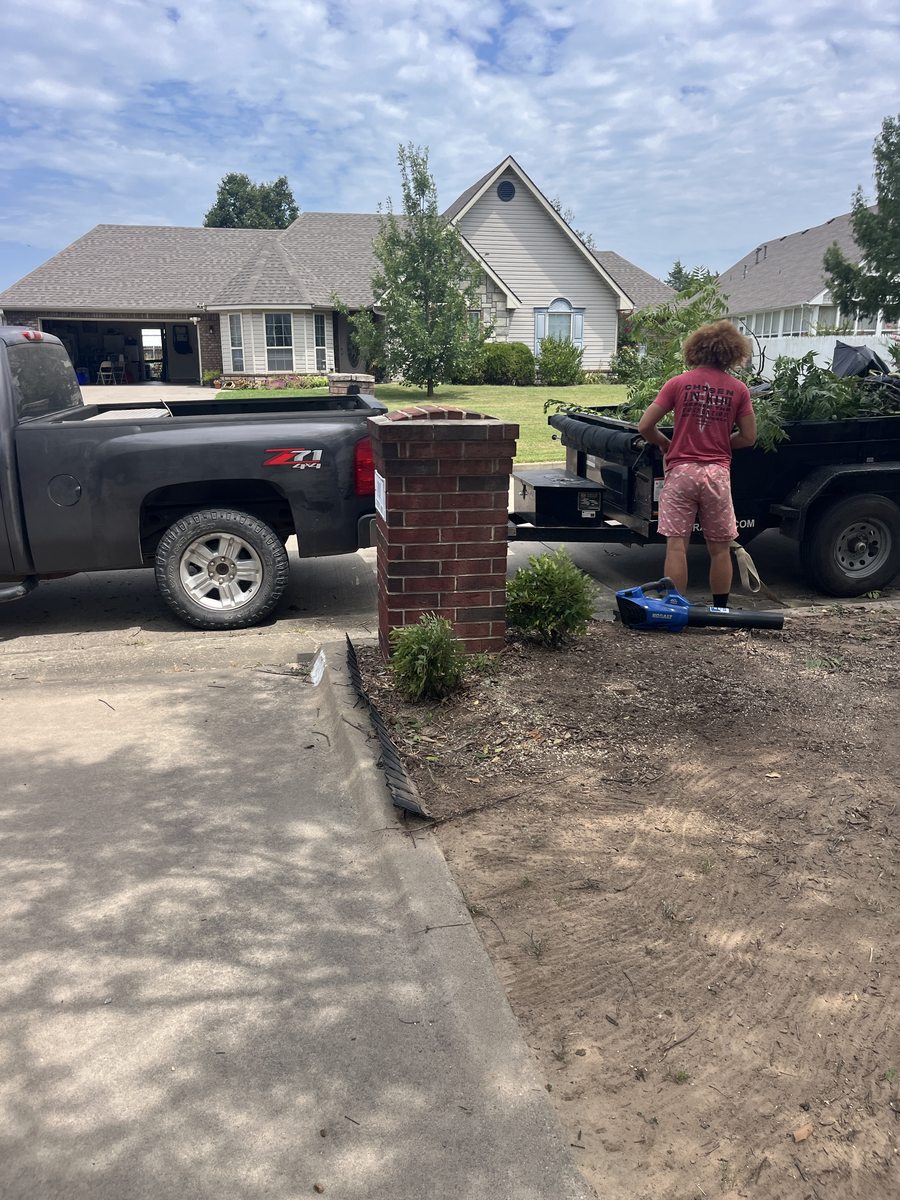 A Barco crew member raking out a cleared bed beside a pickup and trailer on a residential drive.