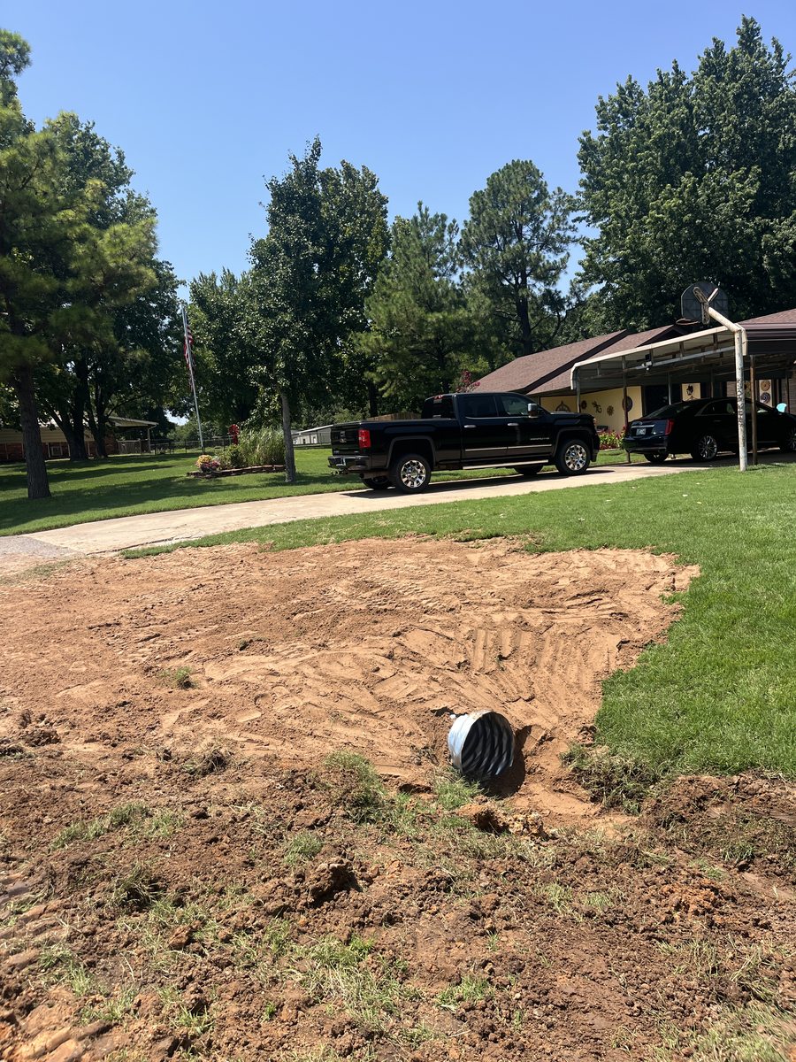 A finished driveway culvert daylighted through fresh graded soil with the lawn edge restored.