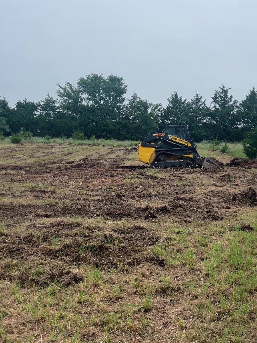 A tracked skid steer working the tree line of a partly cleared Oklahoma field.