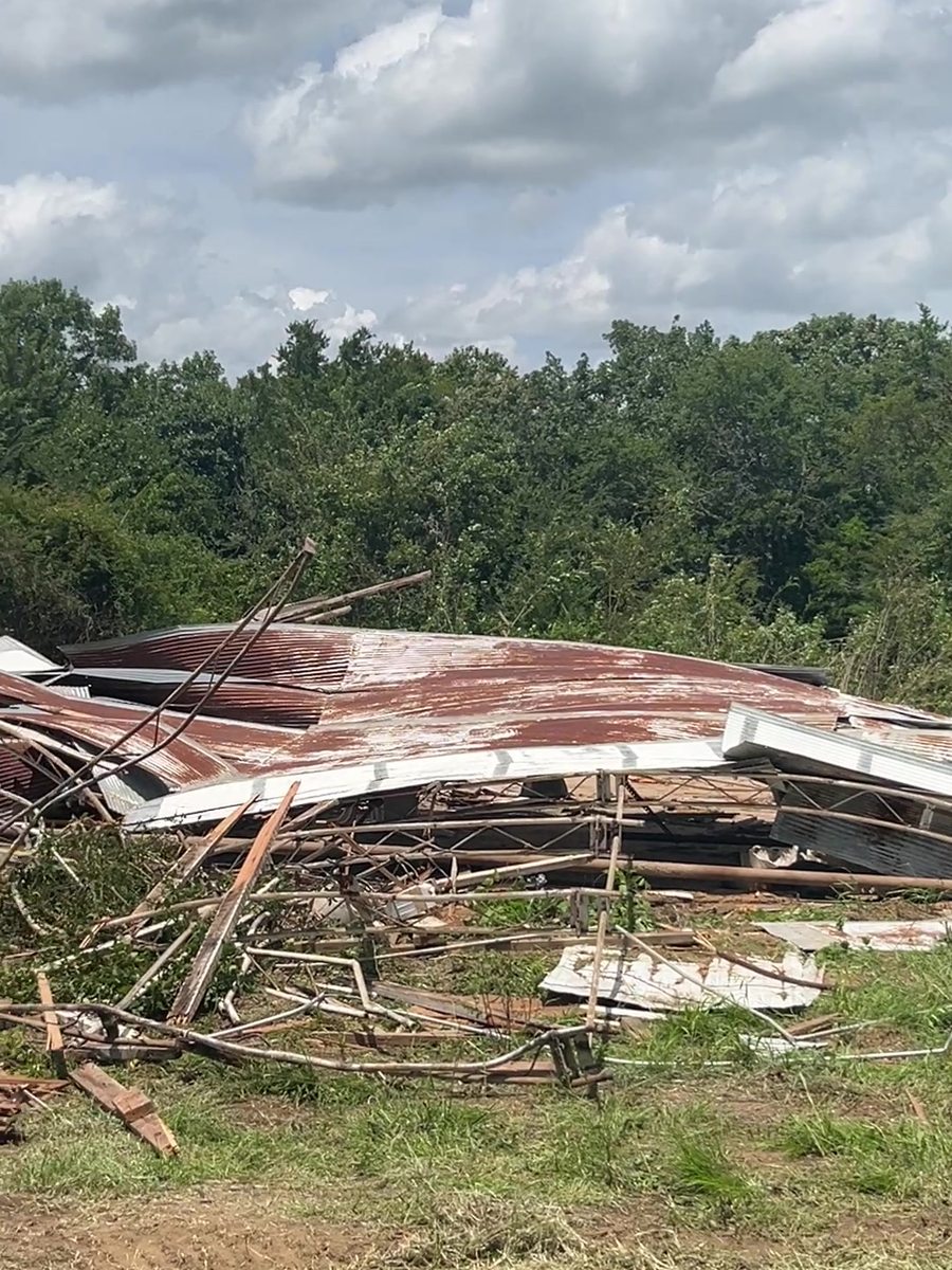 A pile of rusted tin roofing and broken lumber from a demolished metal building, with a dump trailer alongside.